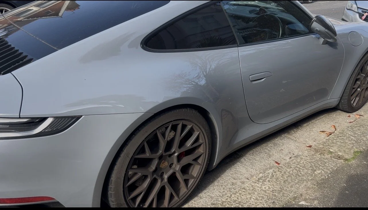 Gray Porsche sports car parked on the side of the road with black rims and a closed door.