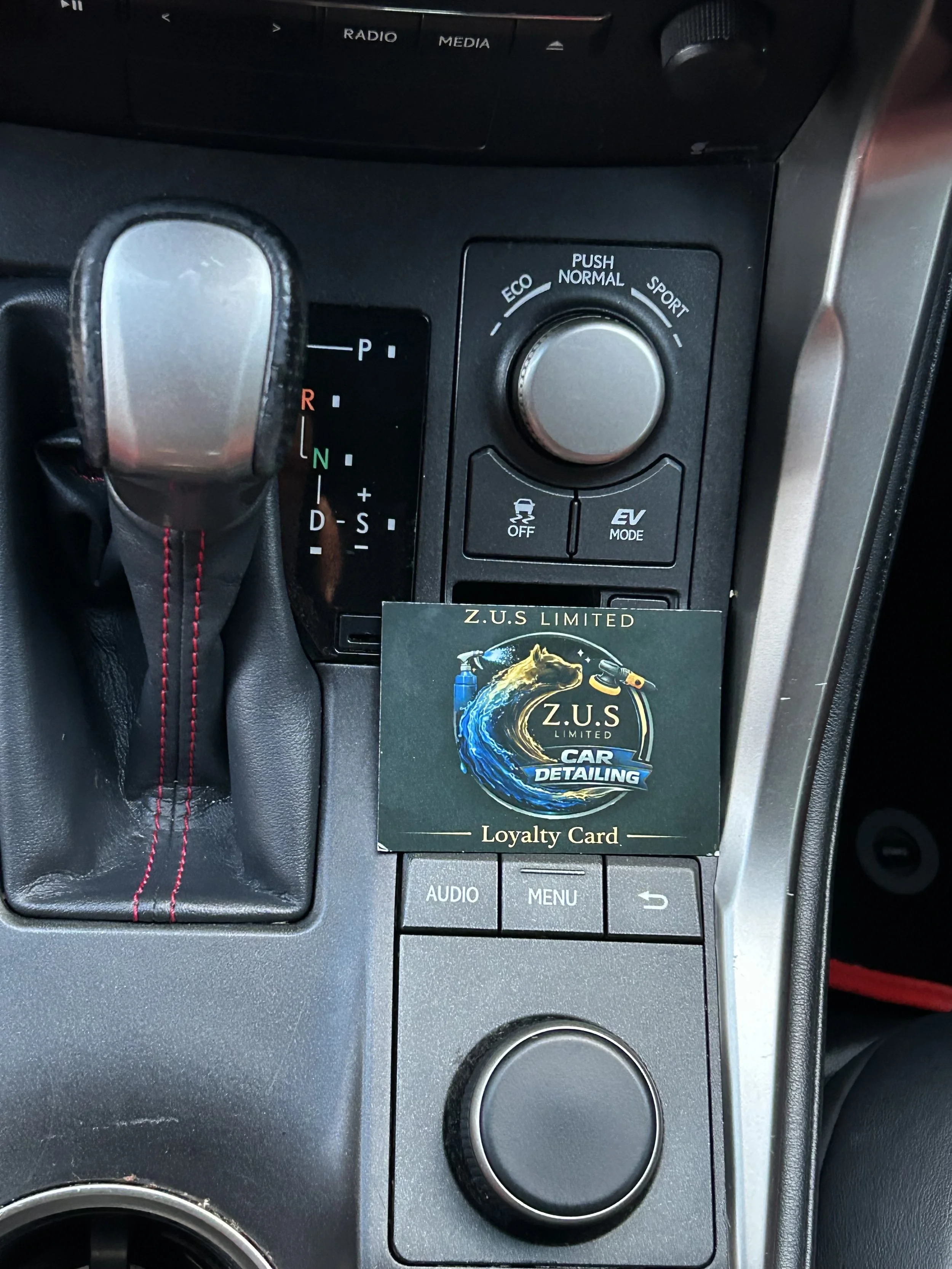 Car interior dashboard with gear shift, control buttons, and a loyalty card on the center console.