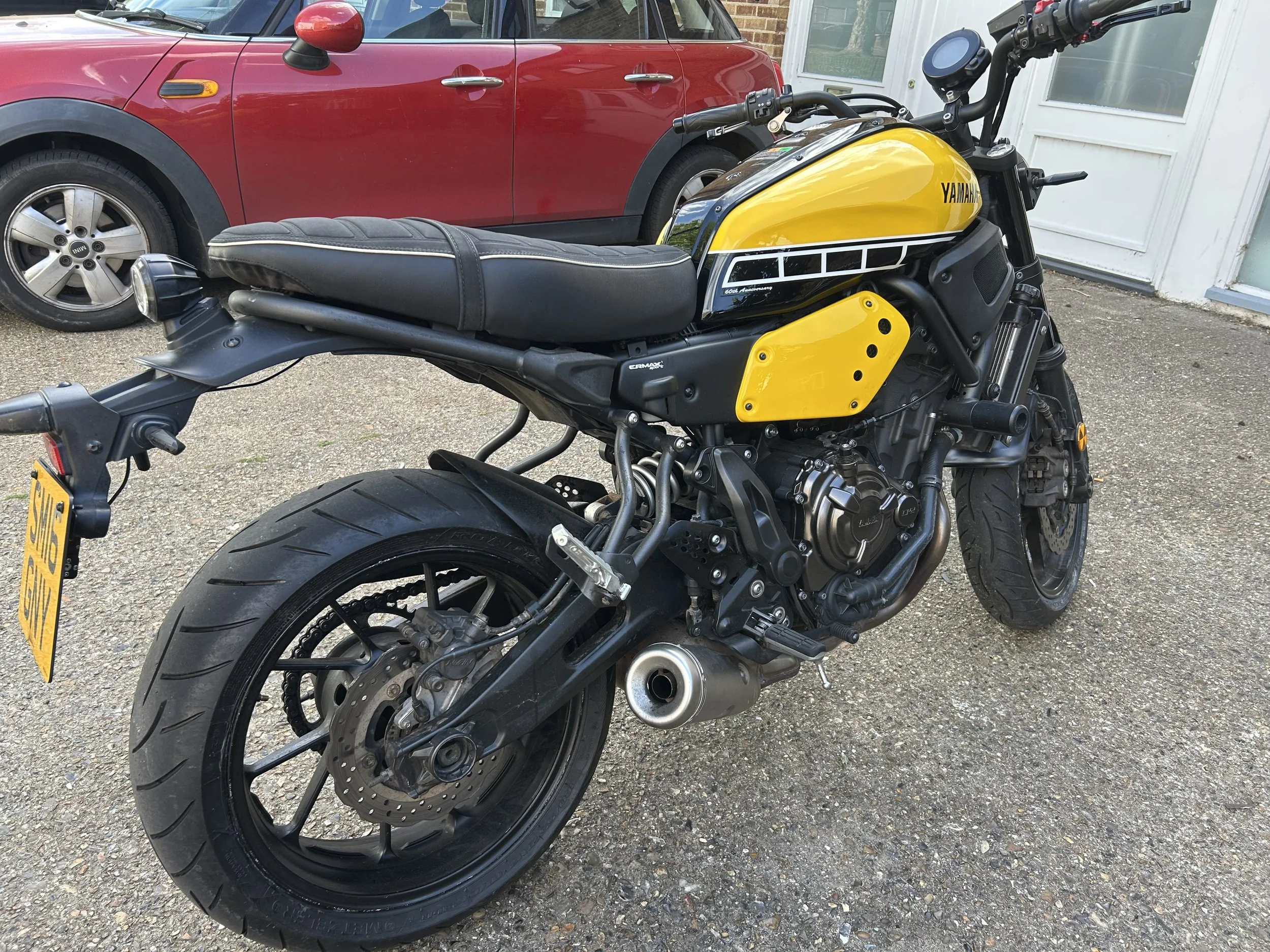 A yellow Yamaha motorcycle parked outdoors next to a red car and white building.