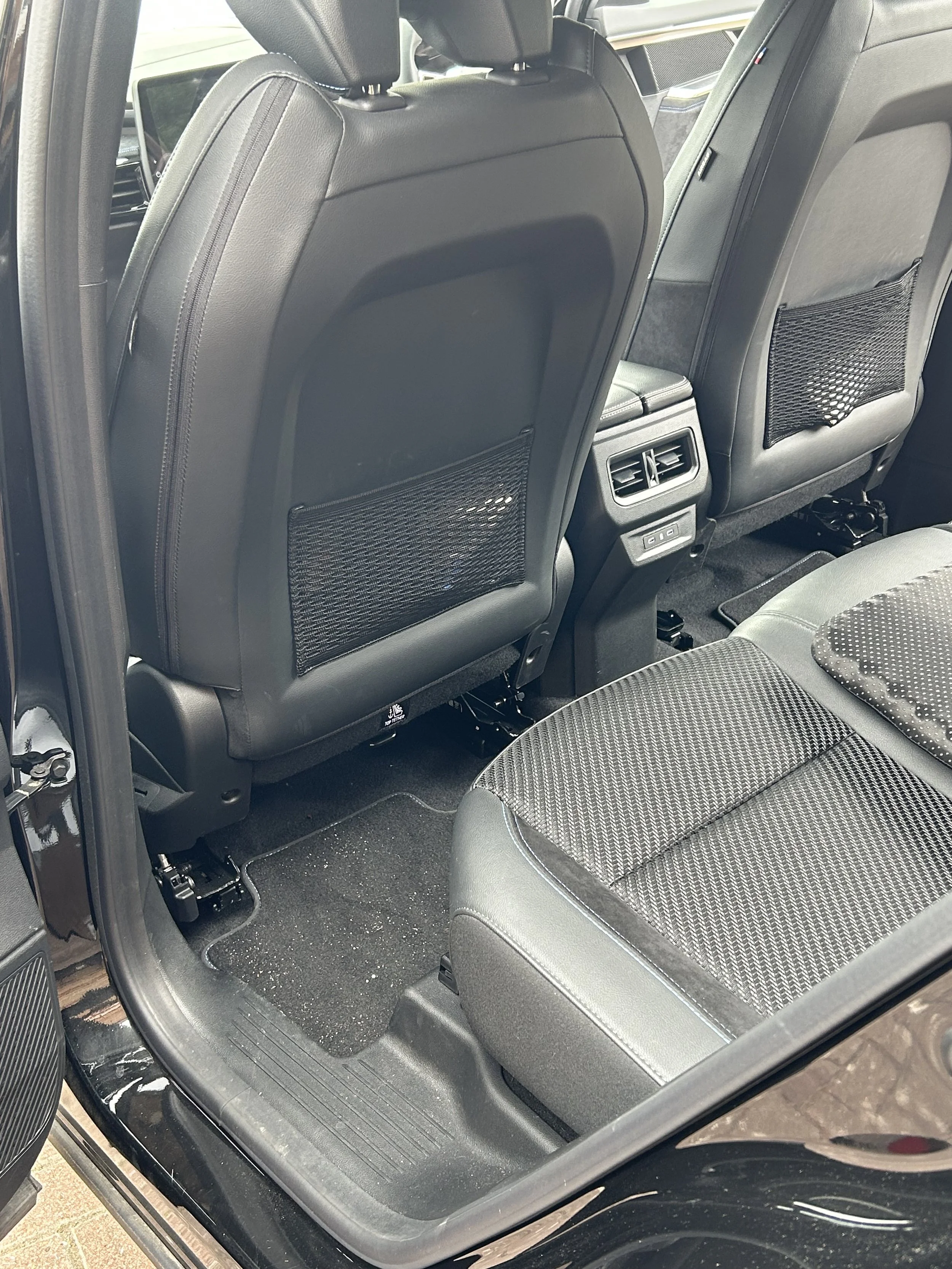 The interior of a car showing the back of the front seats, the back of the driver's seat and the back of the passenger seat, with ventilation vents and controls between the seats, and part of the rear seats visible.