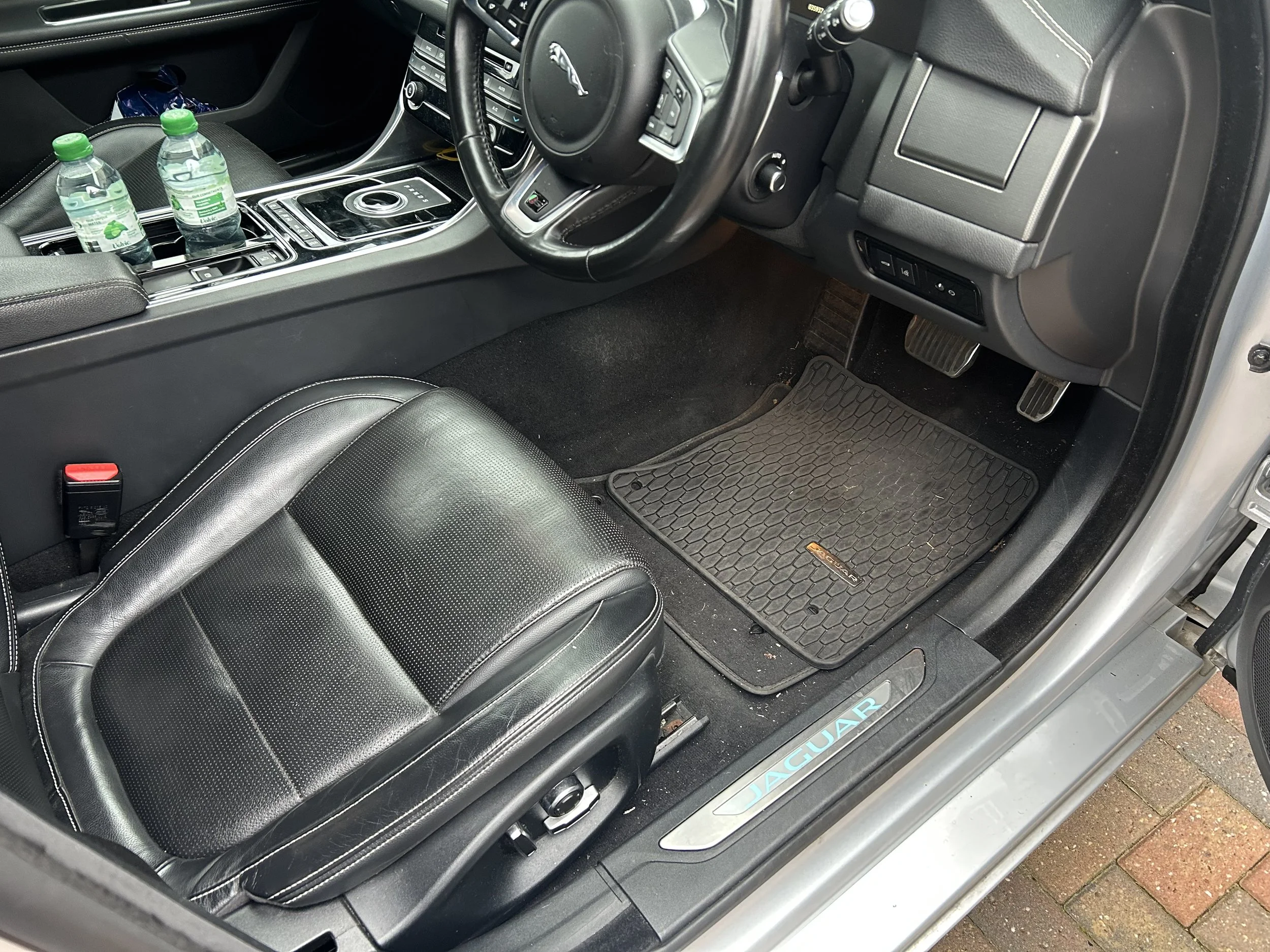 Interior of a luxury Jaguar vehicle with two water bottles on the center console, black leather seats, and a floor mat.