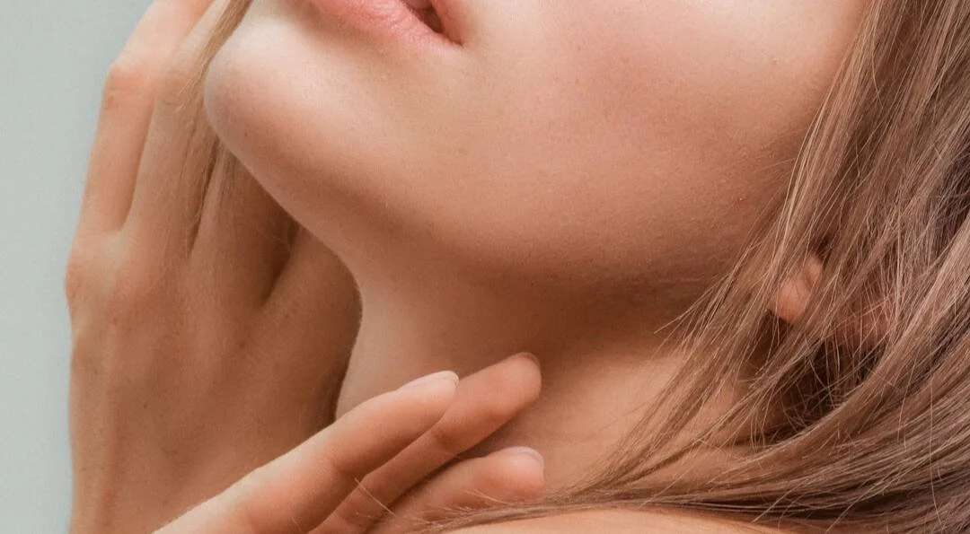 Close-up of a woman's chin, lips, and part of her neck with her hand gently touching her face.