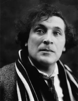Black and white portrait of a man with curly hair, wearing a jacket and a striped scarf.