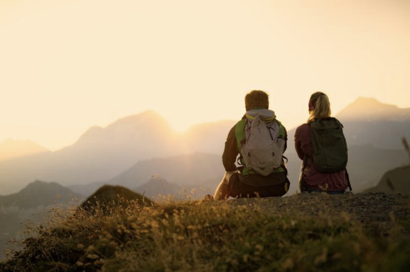 Deux randonneurs assis sur une colline regardant un coucher de soleil sur des montagnes.