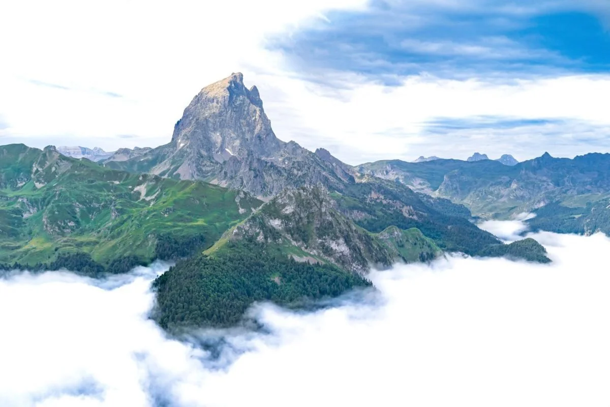 Montagnes vertes avec sommet rocheux entouré de nuages et ciel partiellement couvert.