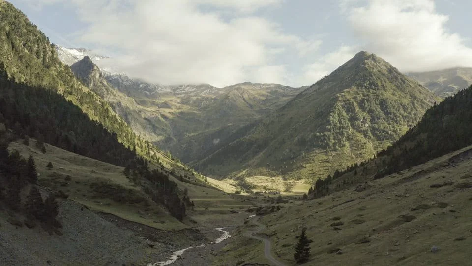 Vue de montagnes verdoyantes avec un canyon, rivière et un ciel partiellement nuageux.