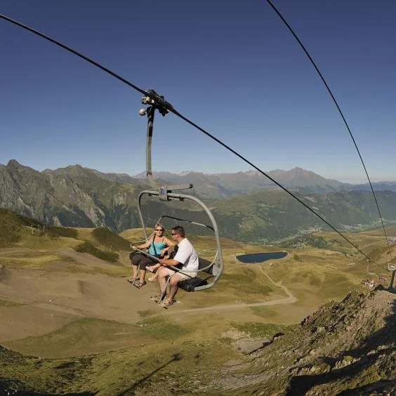 Deux personnes assises sur une chaise dans une télécabine sur une montagne, avec un paysage montagneux en arrière-plan.