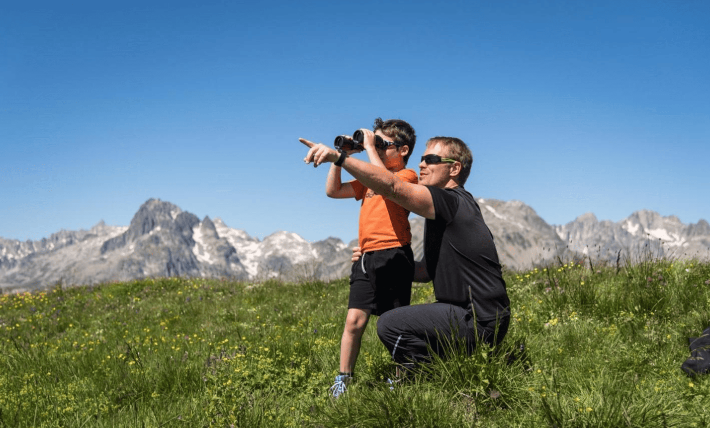 Un homme et un garçon regardant à travers des jumelles dans un paysage de montagne avec un ciel clair.