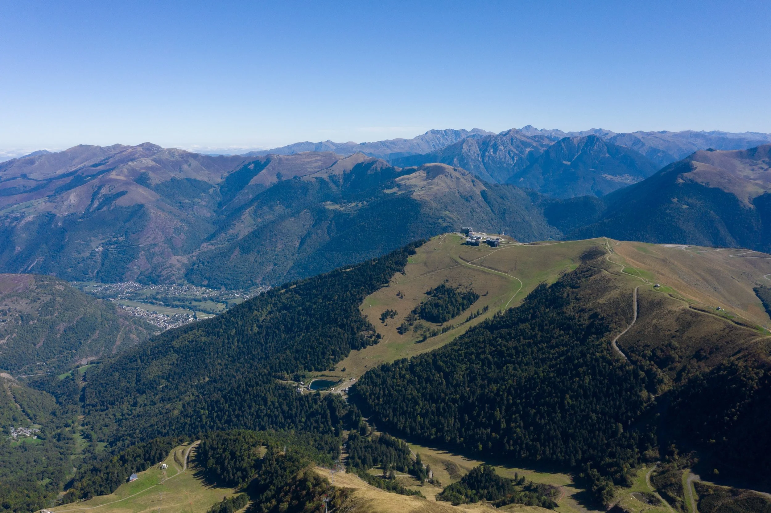 Vue d'une chaîne de montagnes avec des collines verdoyantes, des bâtiments au sommet d'une colline, et un ciel clair.