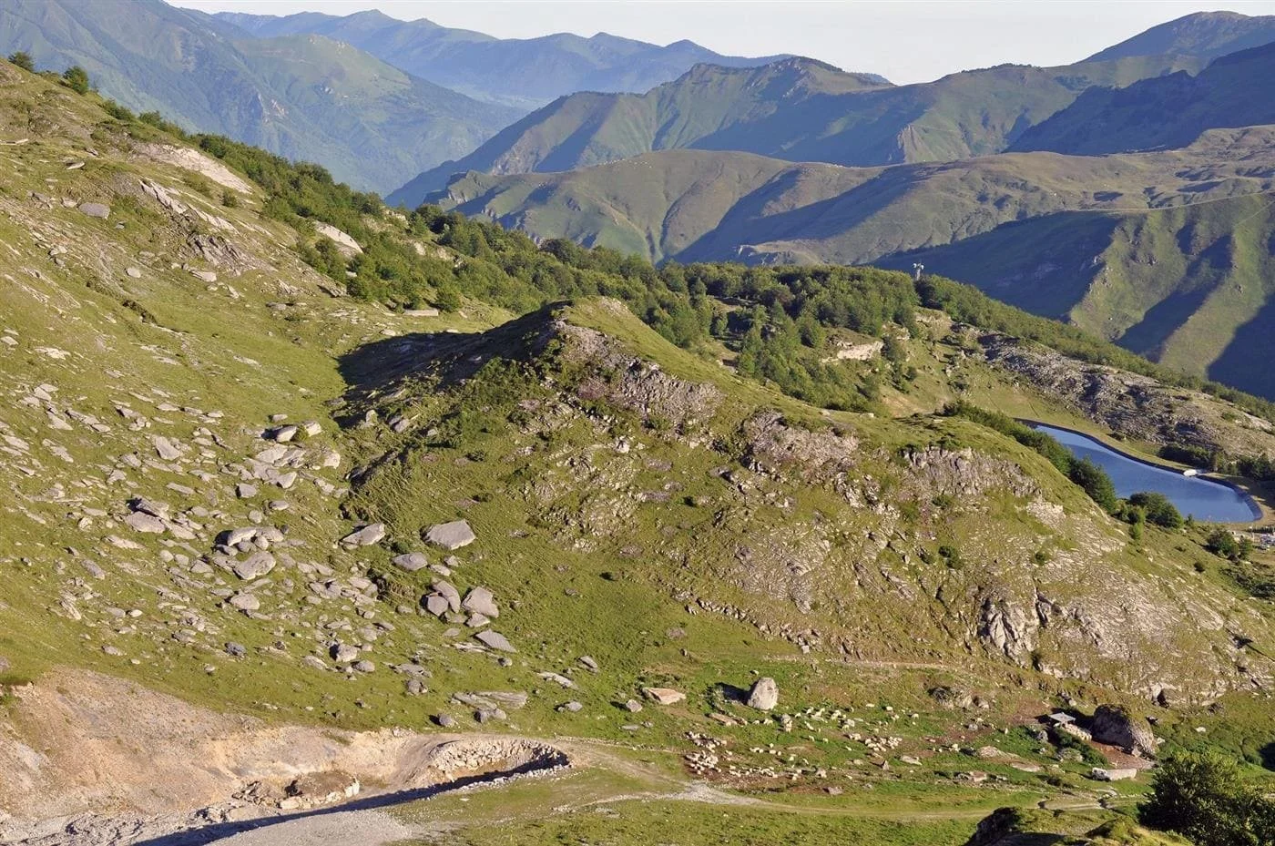 Paysage de montagnes vertes avec des rochers et un lac au fond.
