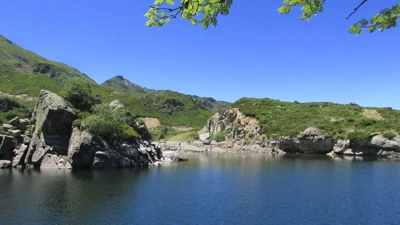 Paysage naturel avec un lac entouré de rochers et de montagnes, ciel bleu et arbres verts.