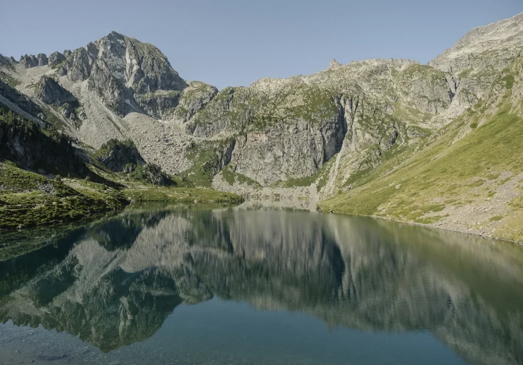 Un lac entouré de montagnes rocheuses et verdoyantes, avec une reflection claire dans l'eau.