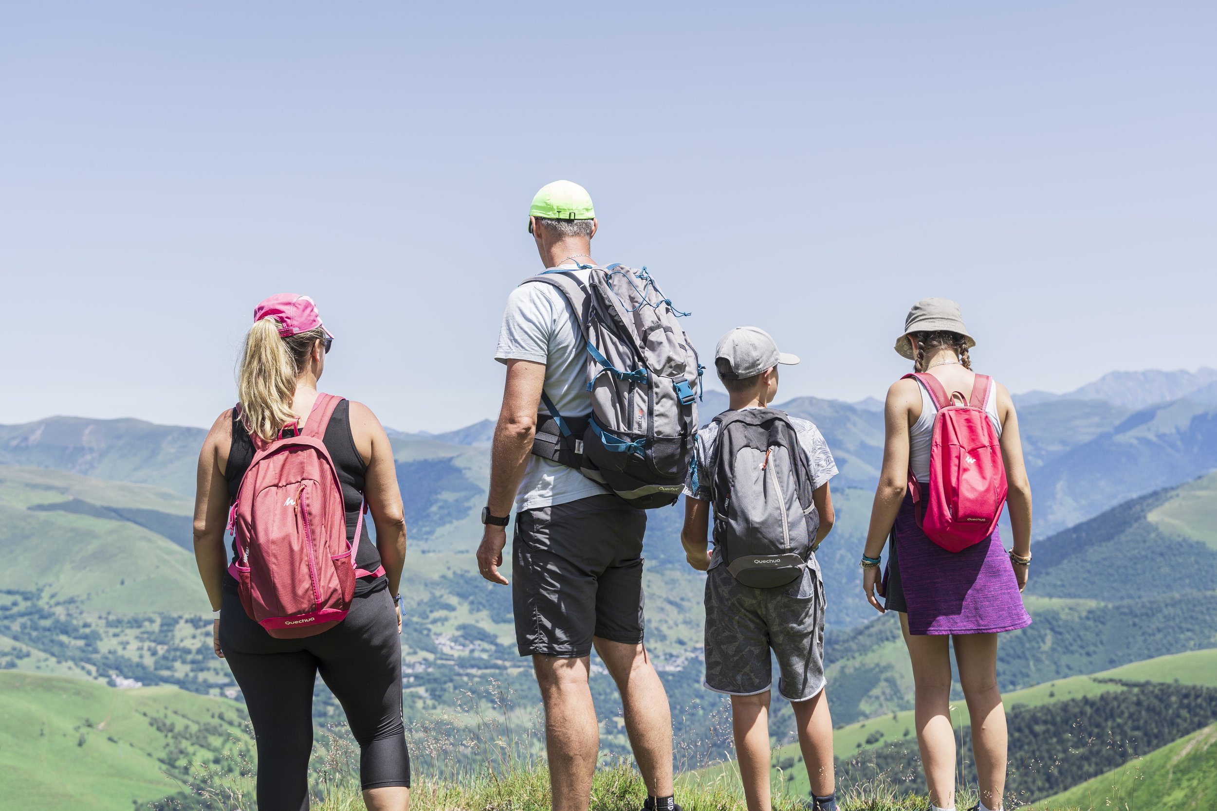 Groupe de cinq randonneurs, dont quatre femmes et un homme, marchant dans un paysage montagneux verdoyant par une journée ensoleillée.