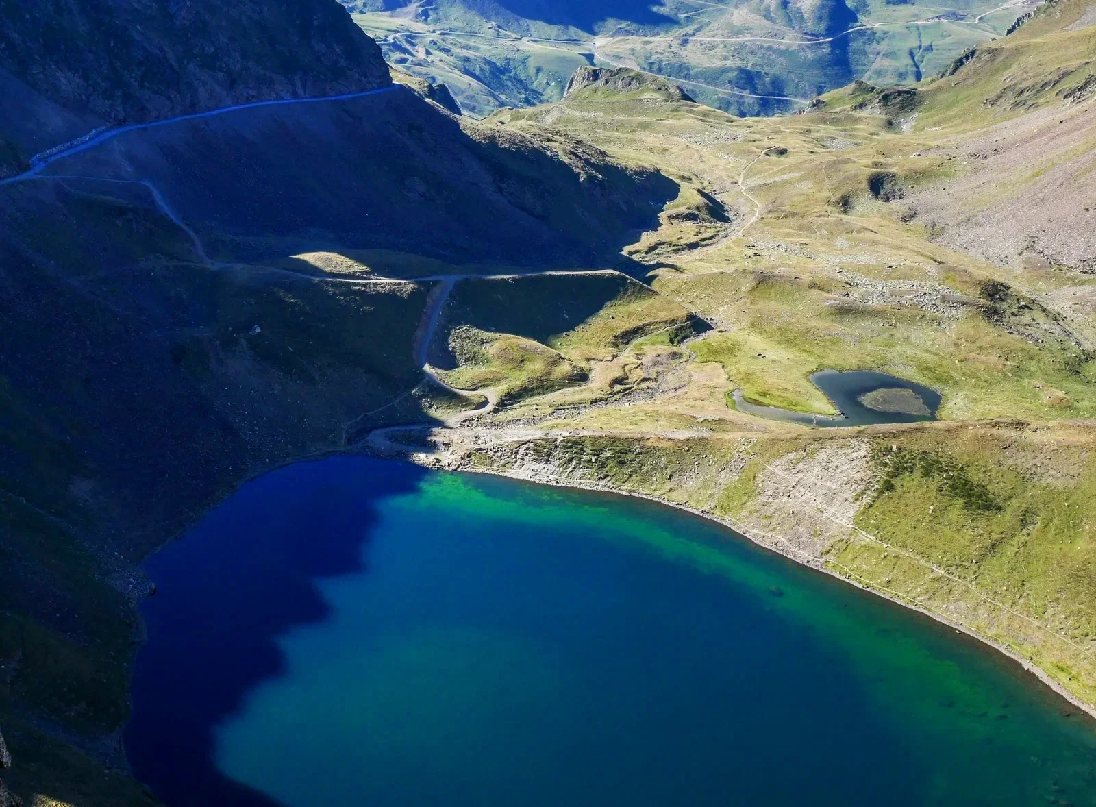 Un lac turquoise entouré de montagnes verdoyantes et de petits étangs dans un paysage alpin.