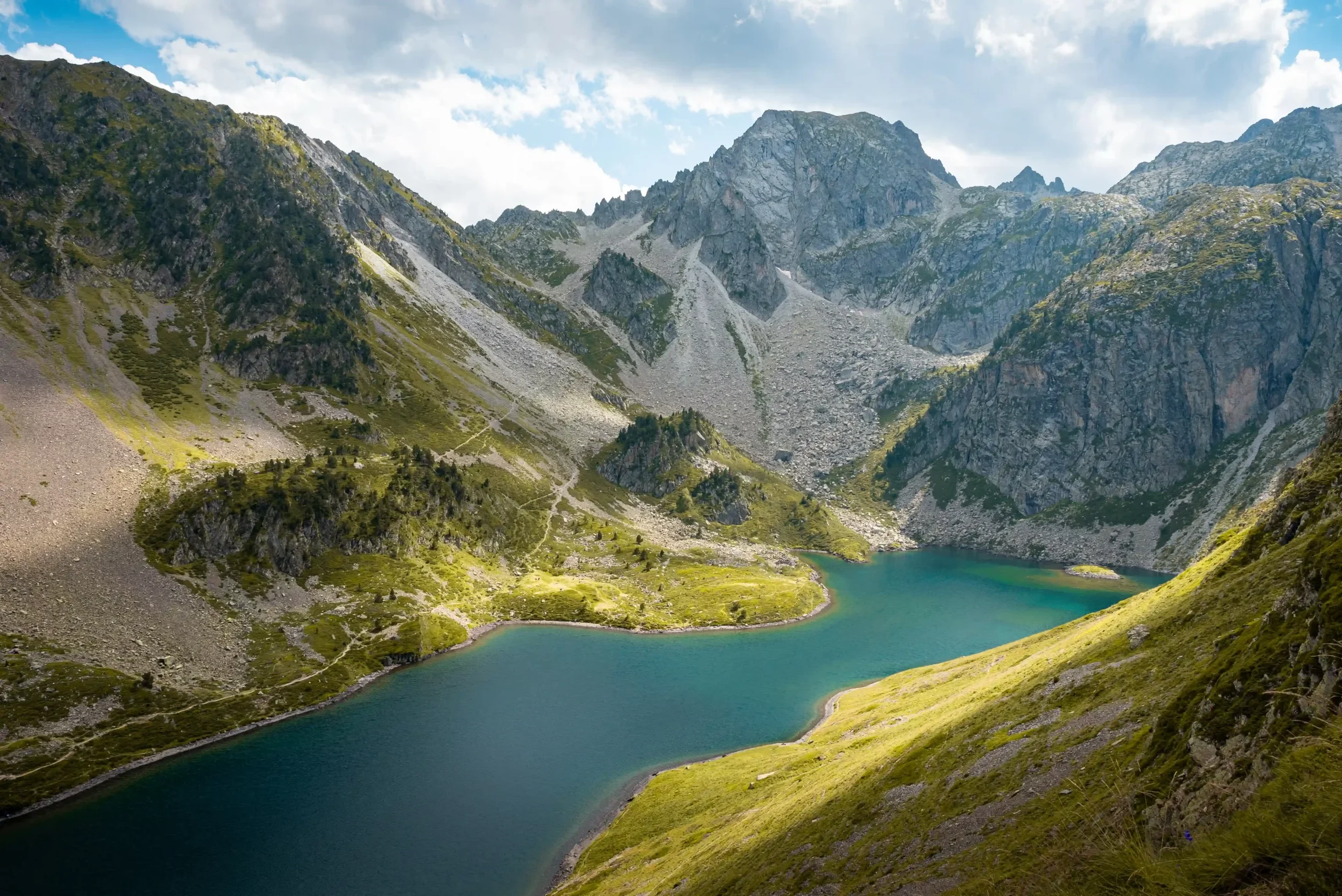 Montagne avec lac turquoise en contrebas, sommets rocheux sous un ciel partiellement nuageux.