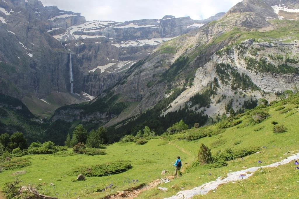 Paysage de montagne avec cascade, forêt, prairie verte, un randonneur avec un sac à dos.