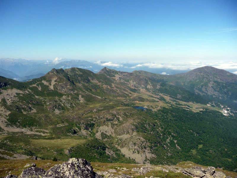 Vue panoramique de montagnes avec sommets rocheux et végétation verte, ciel clair et nuages en arrière-plan.