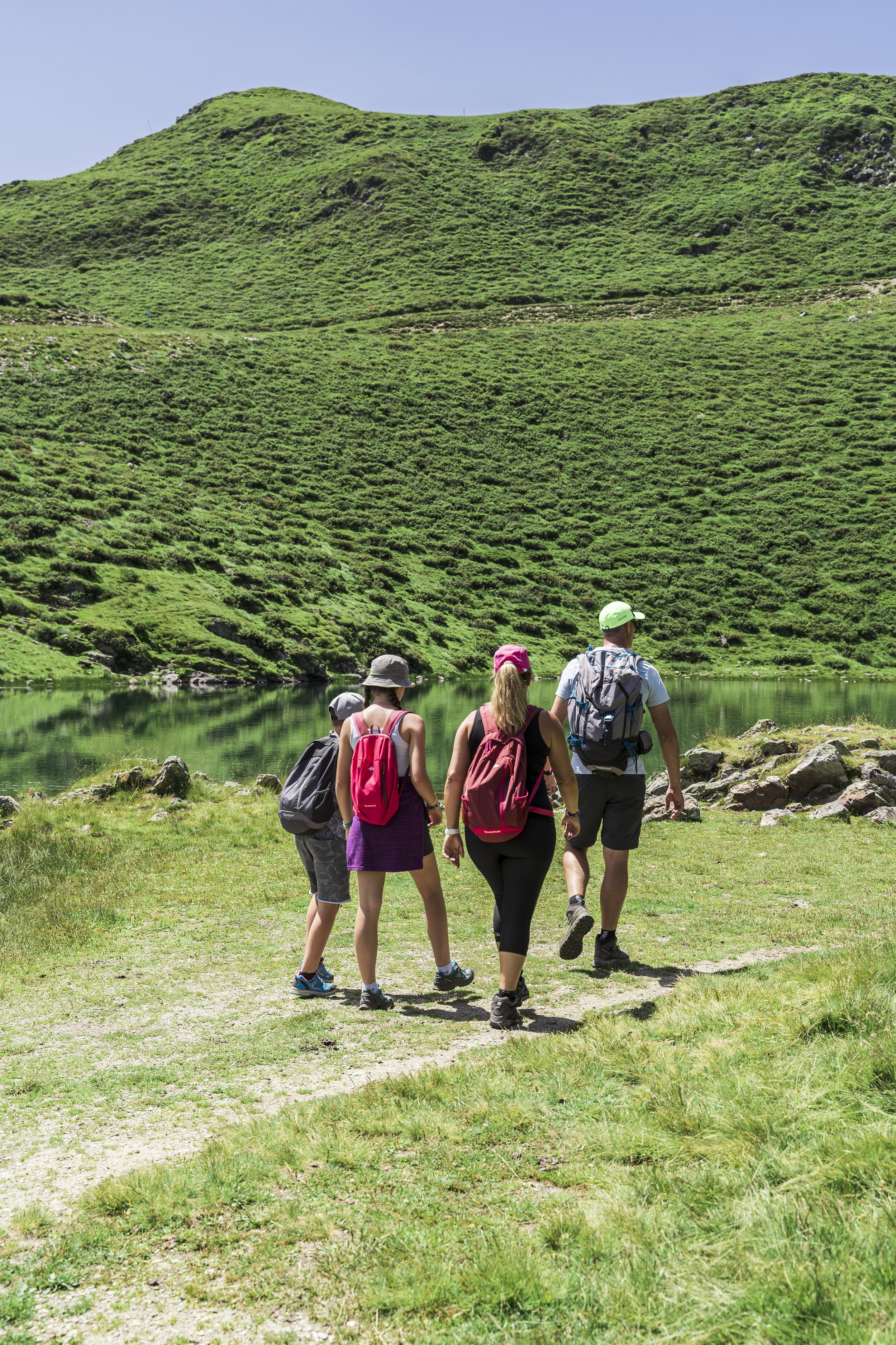 Groupe de randonneurs marchant sur un chemin dans un paysage de montagne verdoyant avec un lac en arrière-plan.