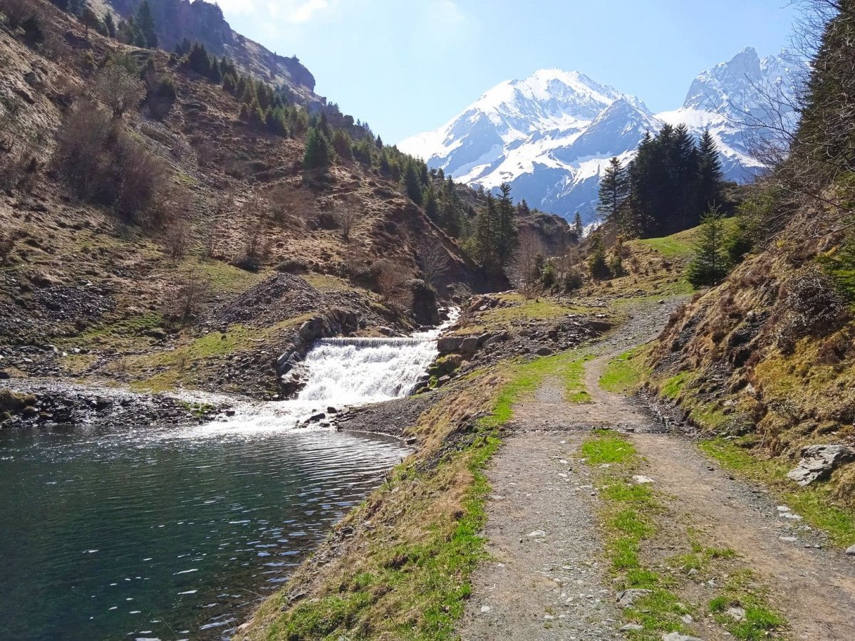 Paysage de montagne avec un lac, une cascade et un chemin en terre, des montagnes enneigées en arrière-plan