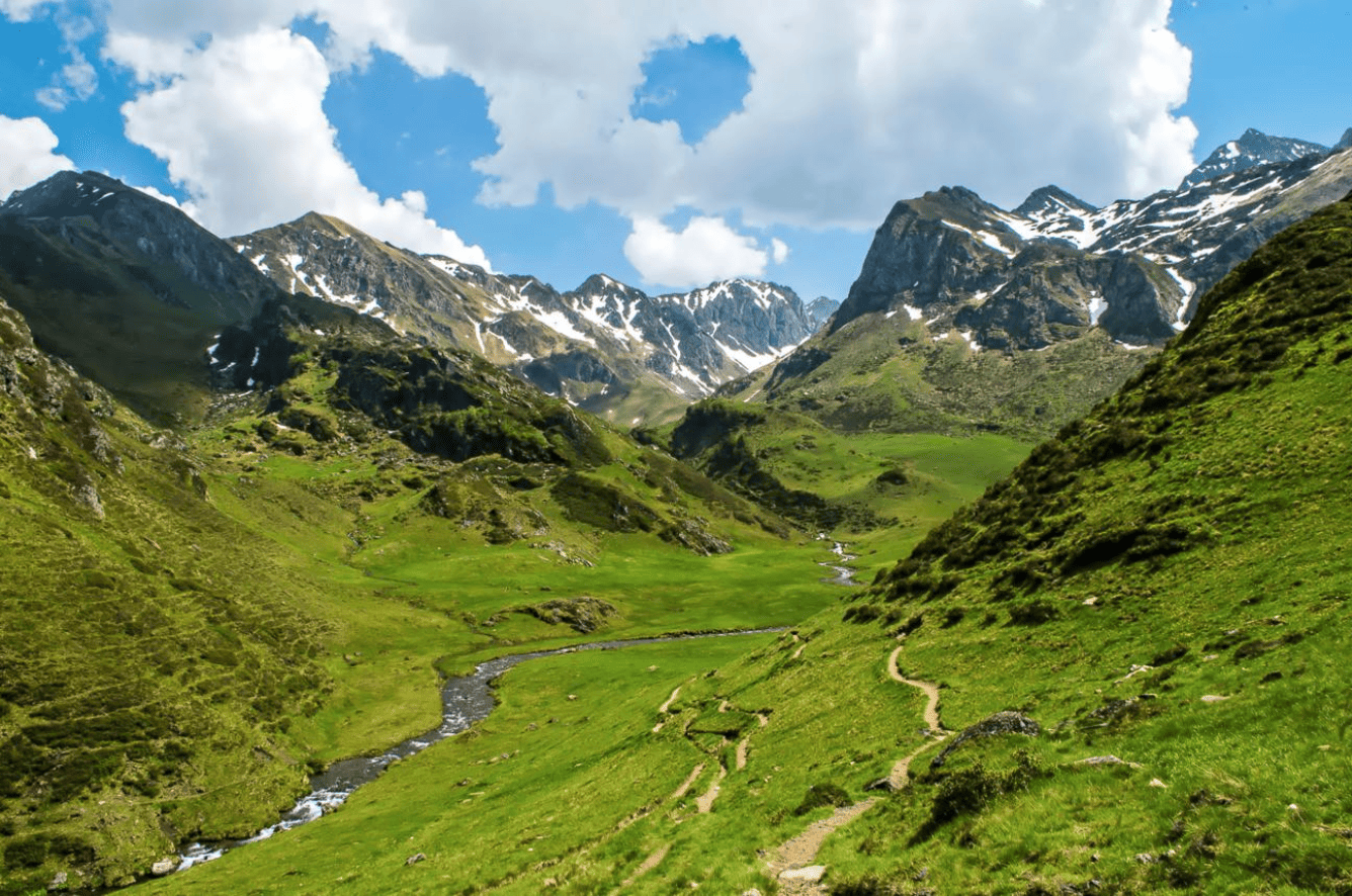 Paysage de montagnes verdoyantes avec un ruisseau serpentant dans la vallée, ciel bleu avec quelques nuages.