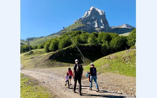 Groupe de quatre personnes marchant sur un sentier en montagne avec une grande montagne en arrière-plan, ciel bleu clair.