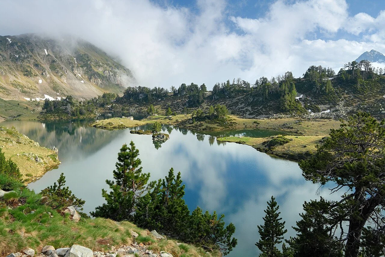 Lac de montagne entouré de forêts et de montagnes avec des nuages dans le ciel.
