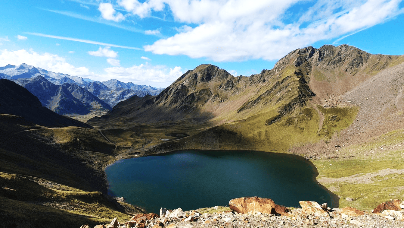 Paysage de montagne avec un lac en contrebas, montagnes escarpées et ciel bleu avec quelques nuages.