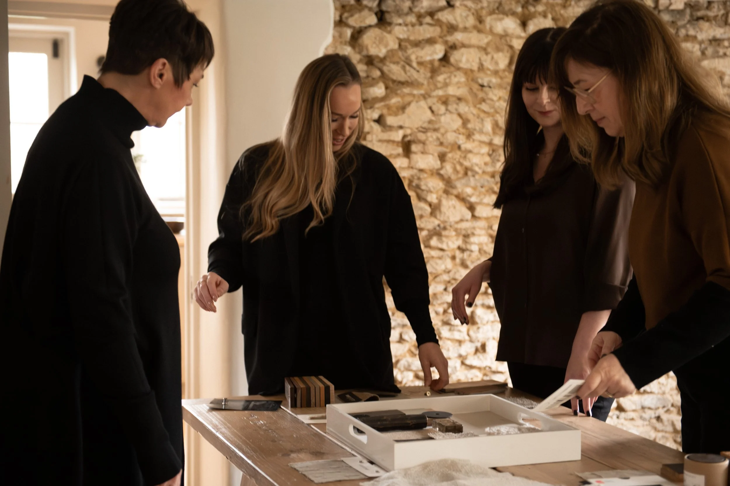 Four members of the Kindly interior design team gathered in discussion beside an exposed stone wall.