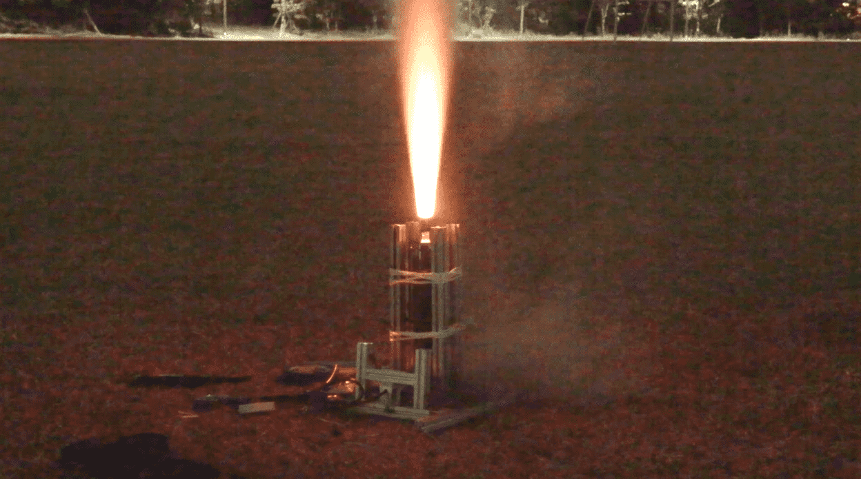 A small rocket launching on a flat, open field at night, with sparks and flame coming out of the top.