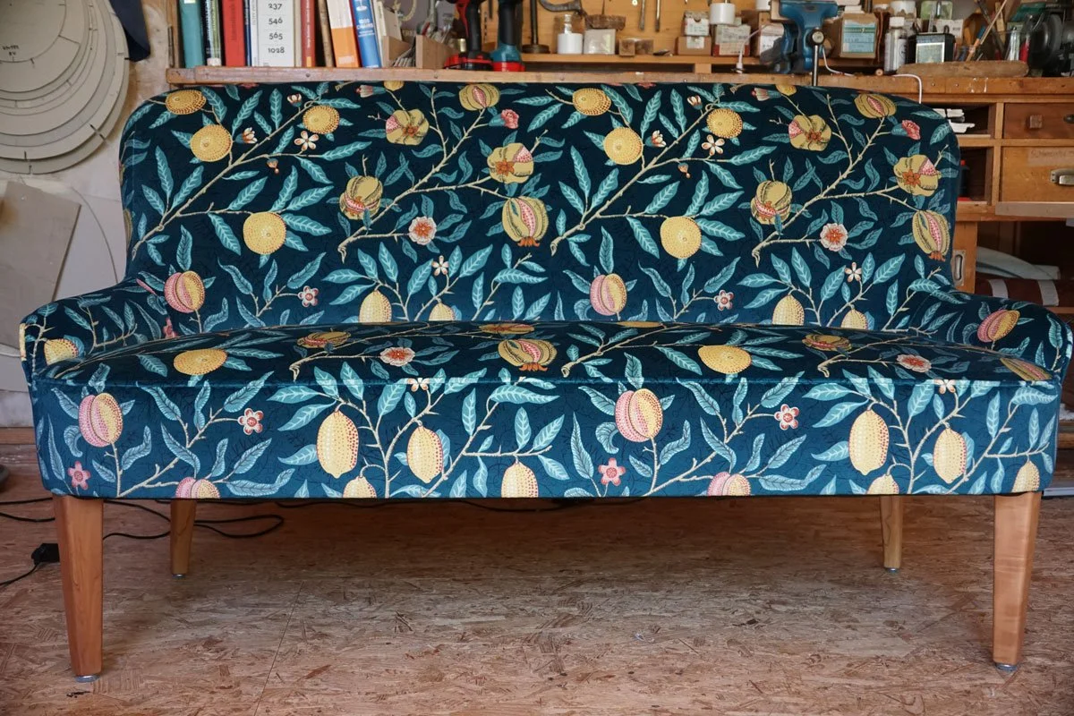 Neu bezogenes Sofa mit farbenfrohem floralem Stoff und Holzfüssen in der Polsterei in der Ostschweiz.