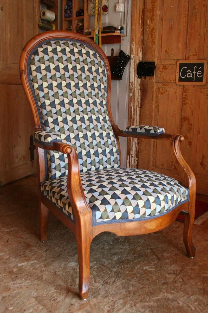 Mit welchem Stoff das Möbel neu polstern? Inspiration: Antiker Armlehnstuhl mit geschwungenem Holzgestell und neuem geometrisch gemustertem Polsterbezug.