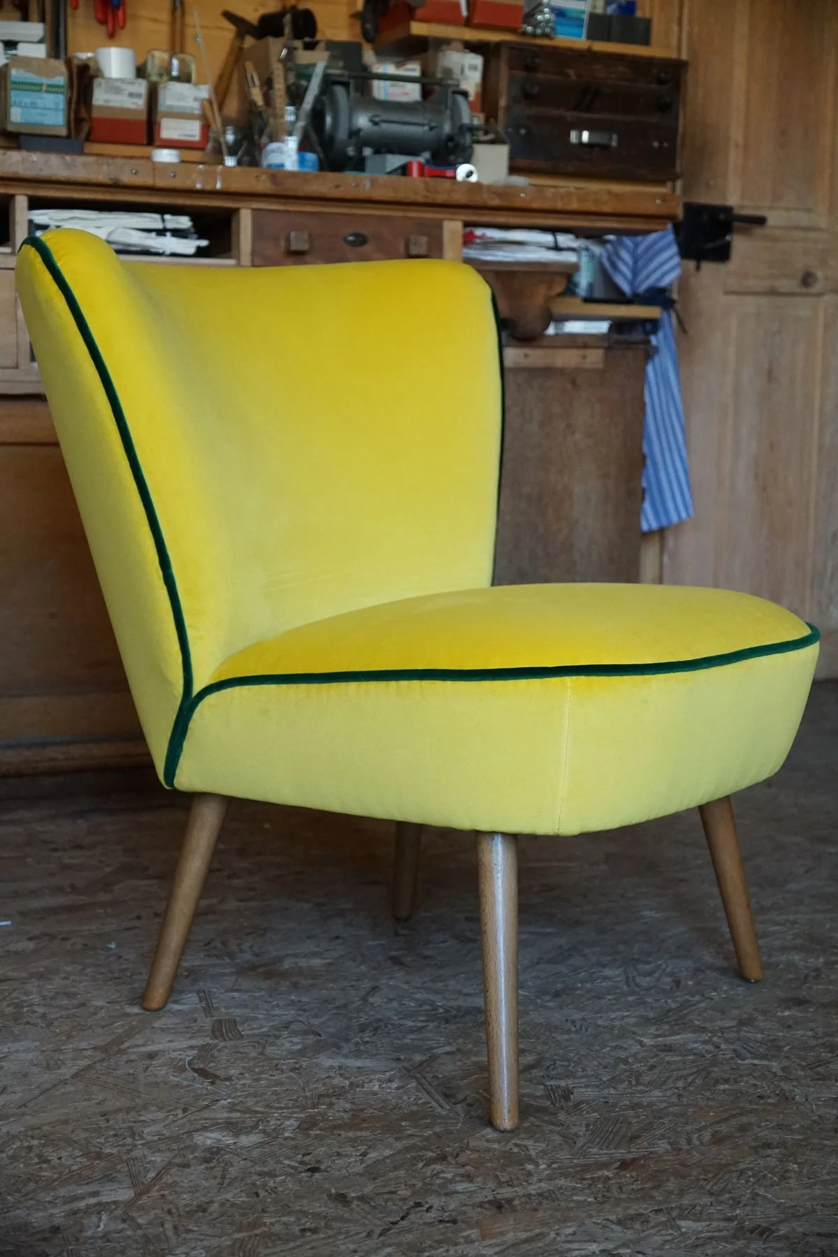 Inspiration aus der Polsterei in der Ostschweiz: Leuchtend gelber Vintage-Sessel mit grüner Paspel und Holzfüssen, frisch bezogen in der Werkstatt Saienbrücke.
