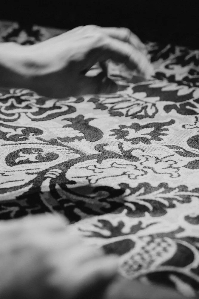 Detail eines kunstvoll gemusterten Polsterstoffs beim Beziehen eines Möbelstücks – sorgfältige Stoffauswahl und traditionelles Polsterhandwerk für alte Sessel und Sofas.