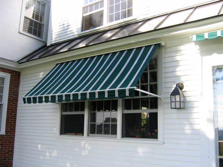 A house with white siding, a striped green and white awning over a window, and a black outdoor wall lantern.