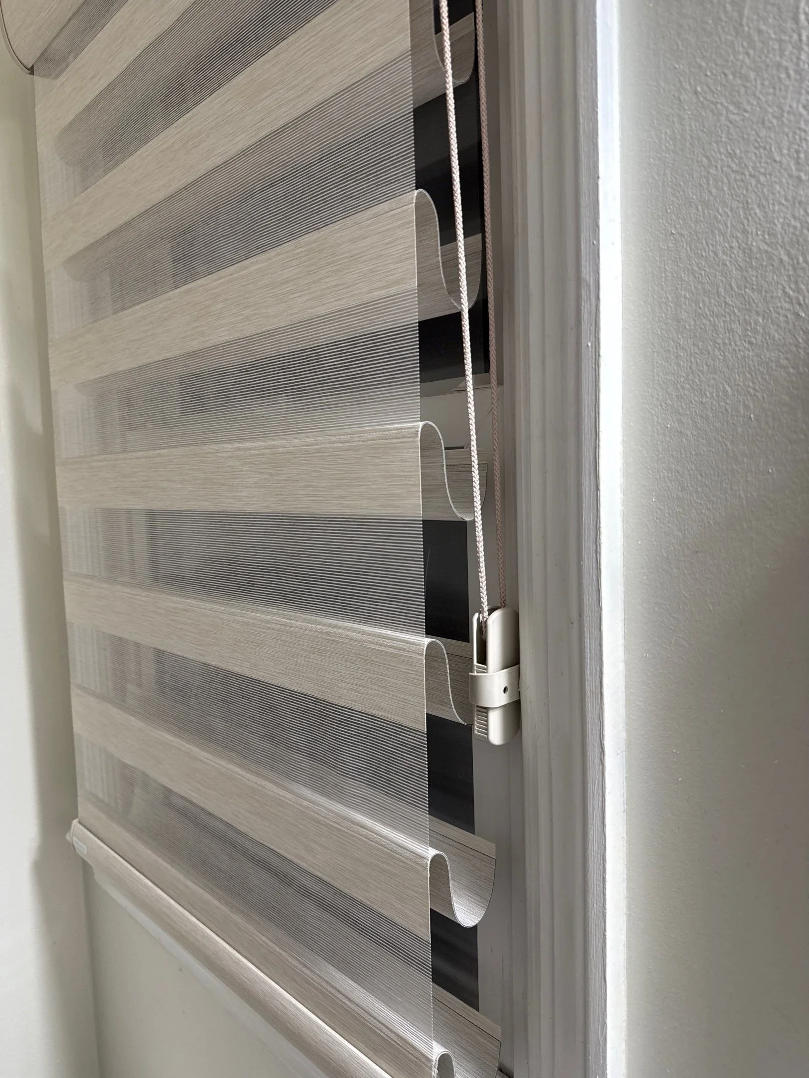 Close-up of a partially lowered horizontal window blind with white cords, mounted on a white wall.