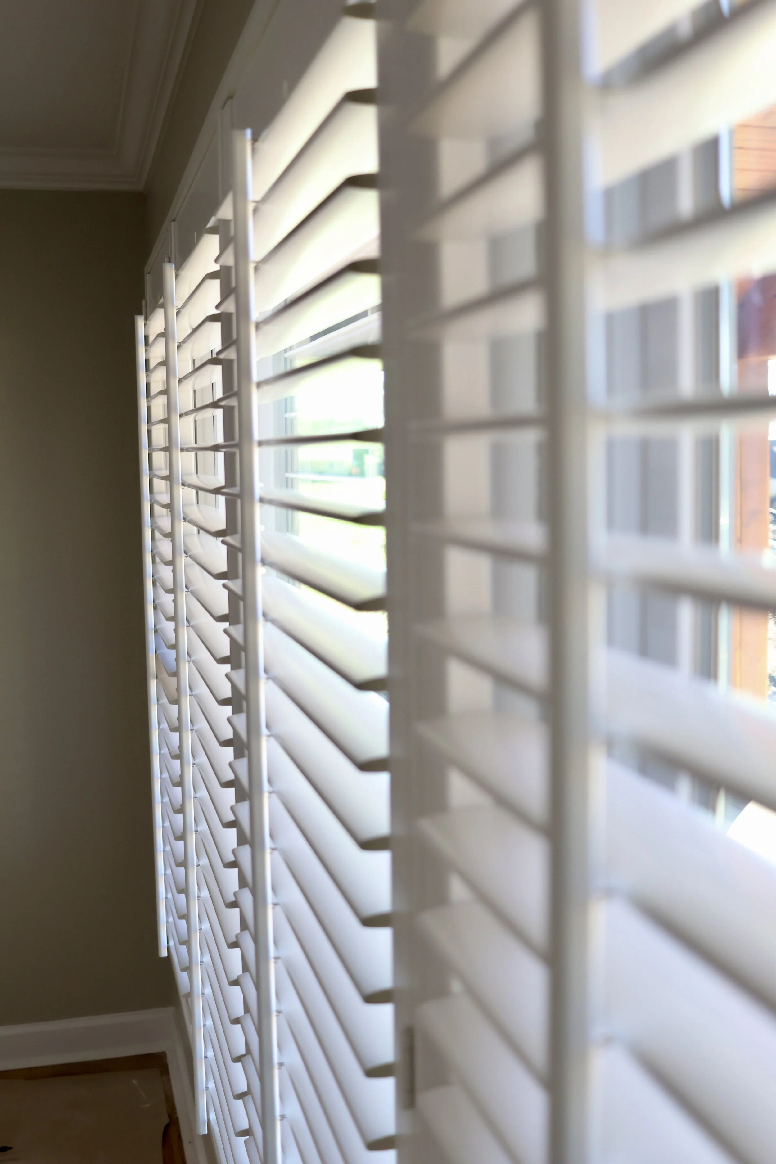 A close-up of white window blinds partially open, with some sunlight coming through.