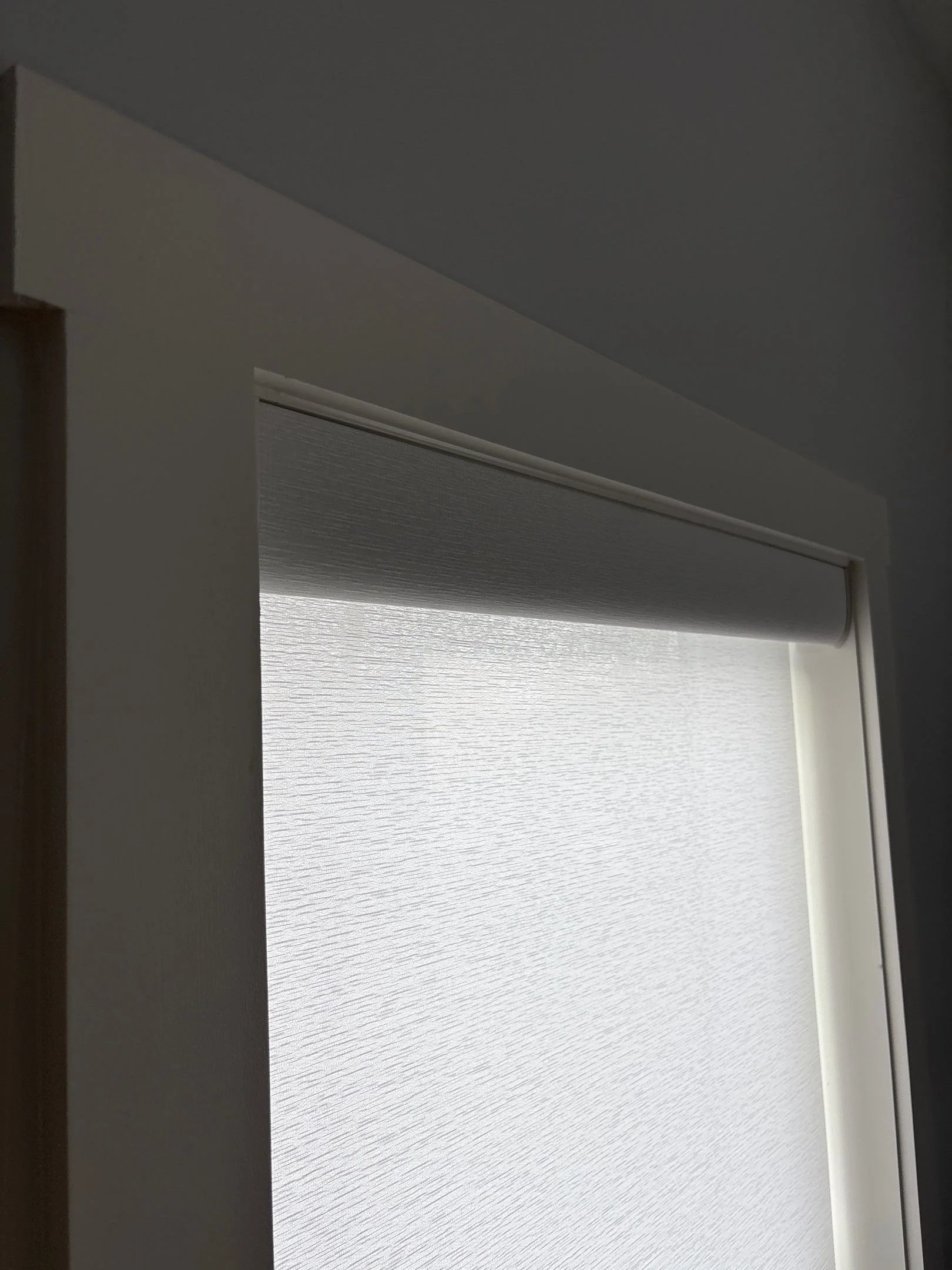 Part of an interior door with a textured window blind and a white wall.
