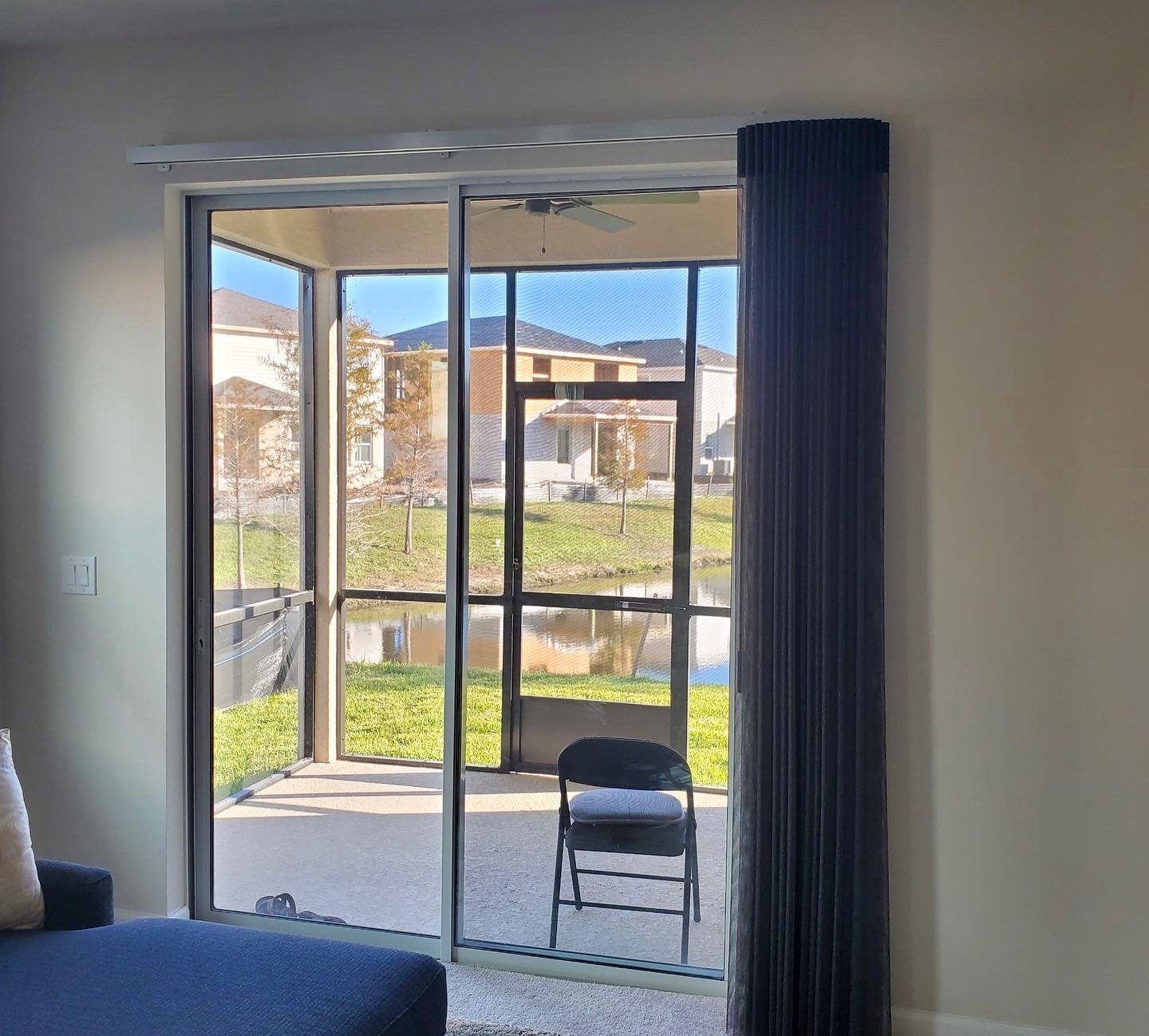 Living room with sliding glass door leading to a screened patio, a chair outside, and a view of houses and trees across a small pond.