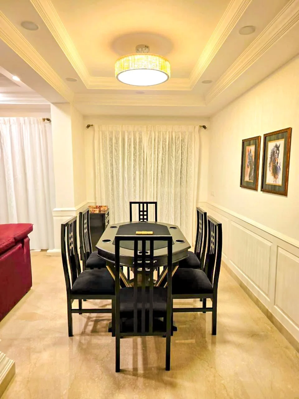 Dining room with a black table and matching chairs, white walls with two framed horse paintings, beige curtains, and a ceiling light fixture.