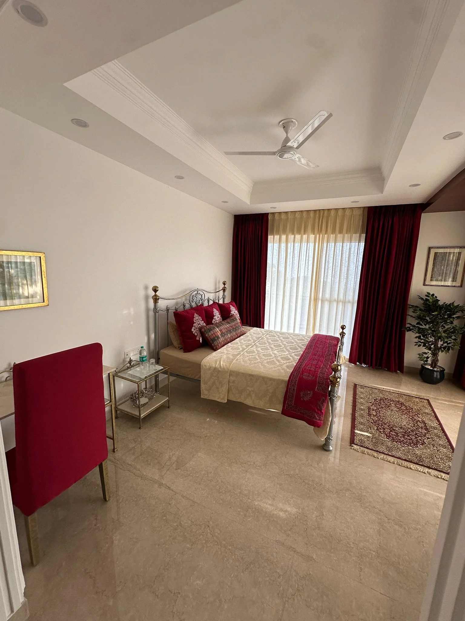 Hotel room with a bed, curtains, balcony, potted plant, and patterned sofa.