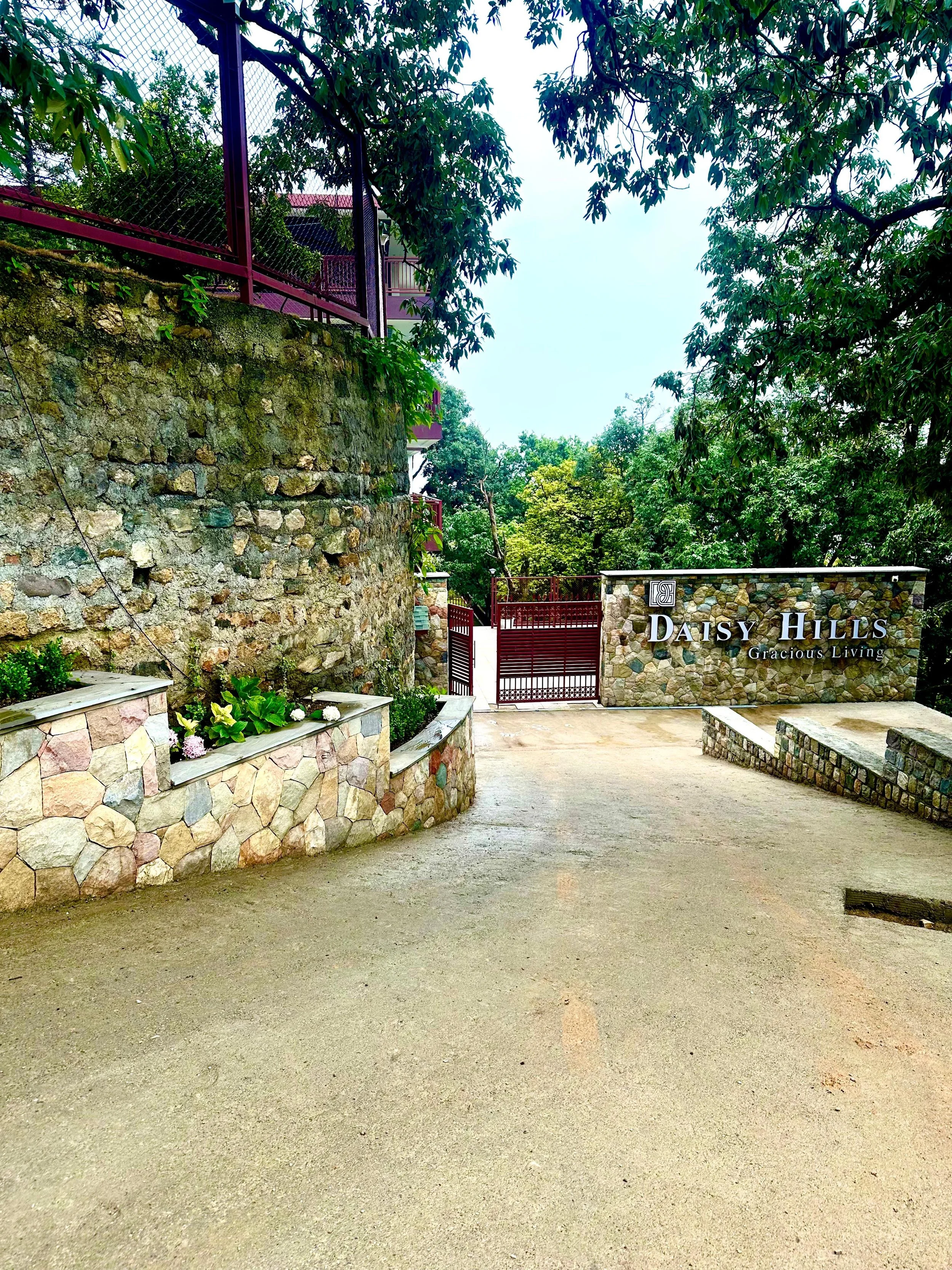 Entrance to Daisy Hills residential community with stone walls, a gate, and lush green trees.
