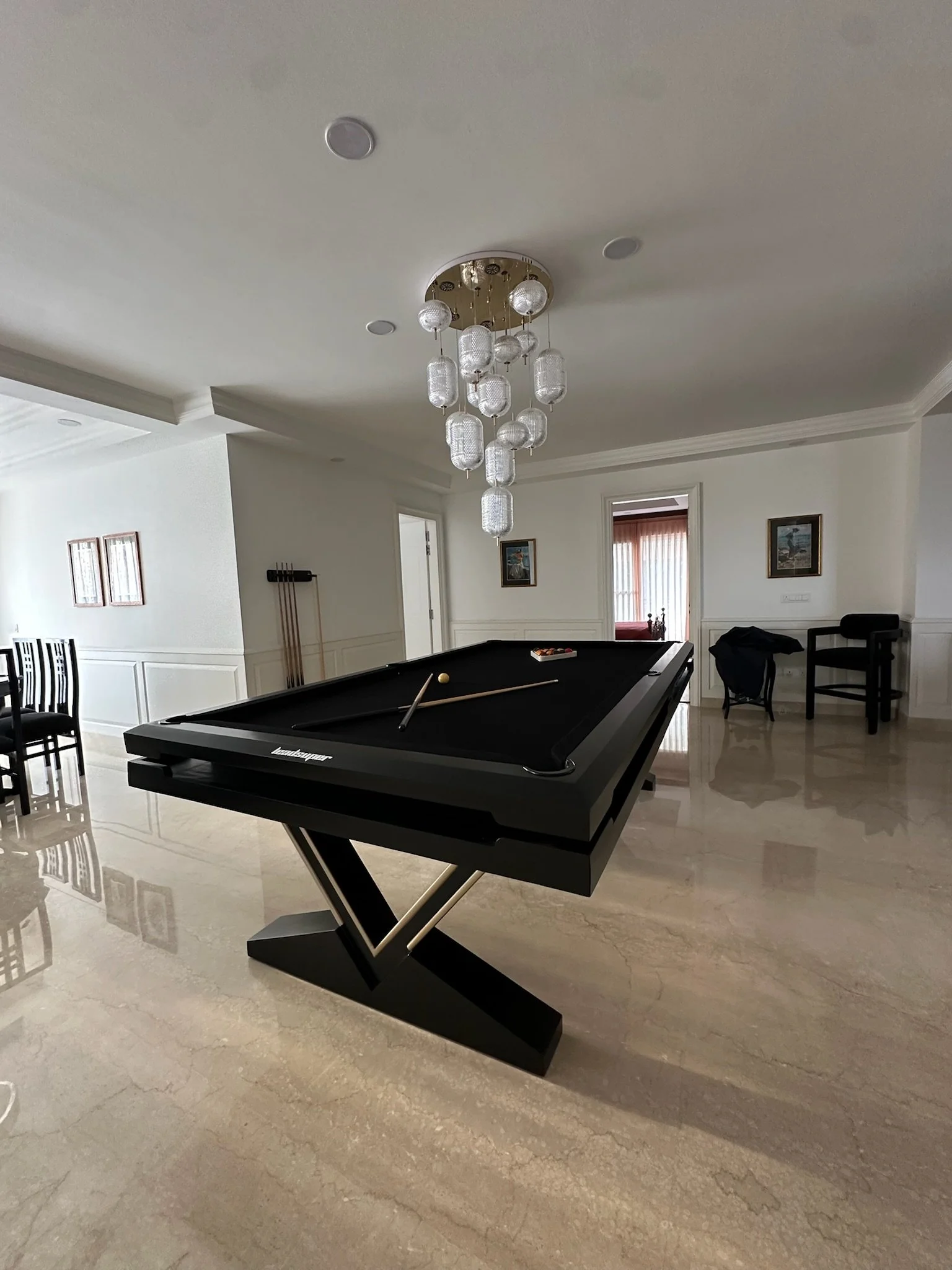 Dining room with a black table and matching chairs, white walls with two framed horse paintings, beige curtains, and a ceiling light fixture.