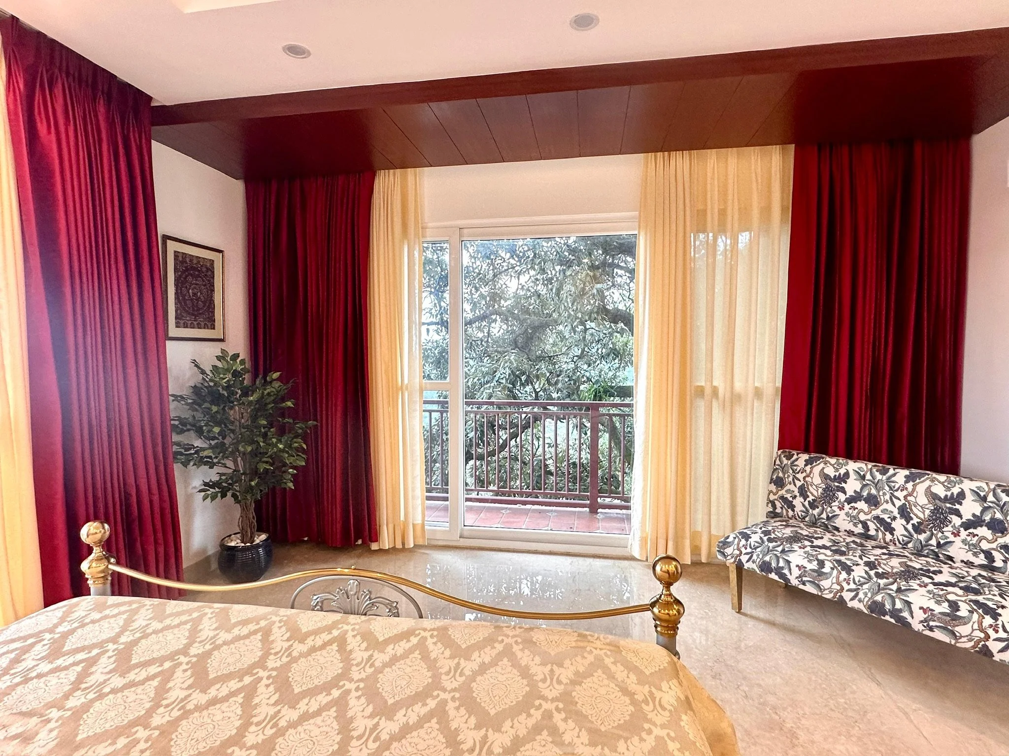 Hotel room with a bed, curtains, balcony, potted plant, and patterned sofa.