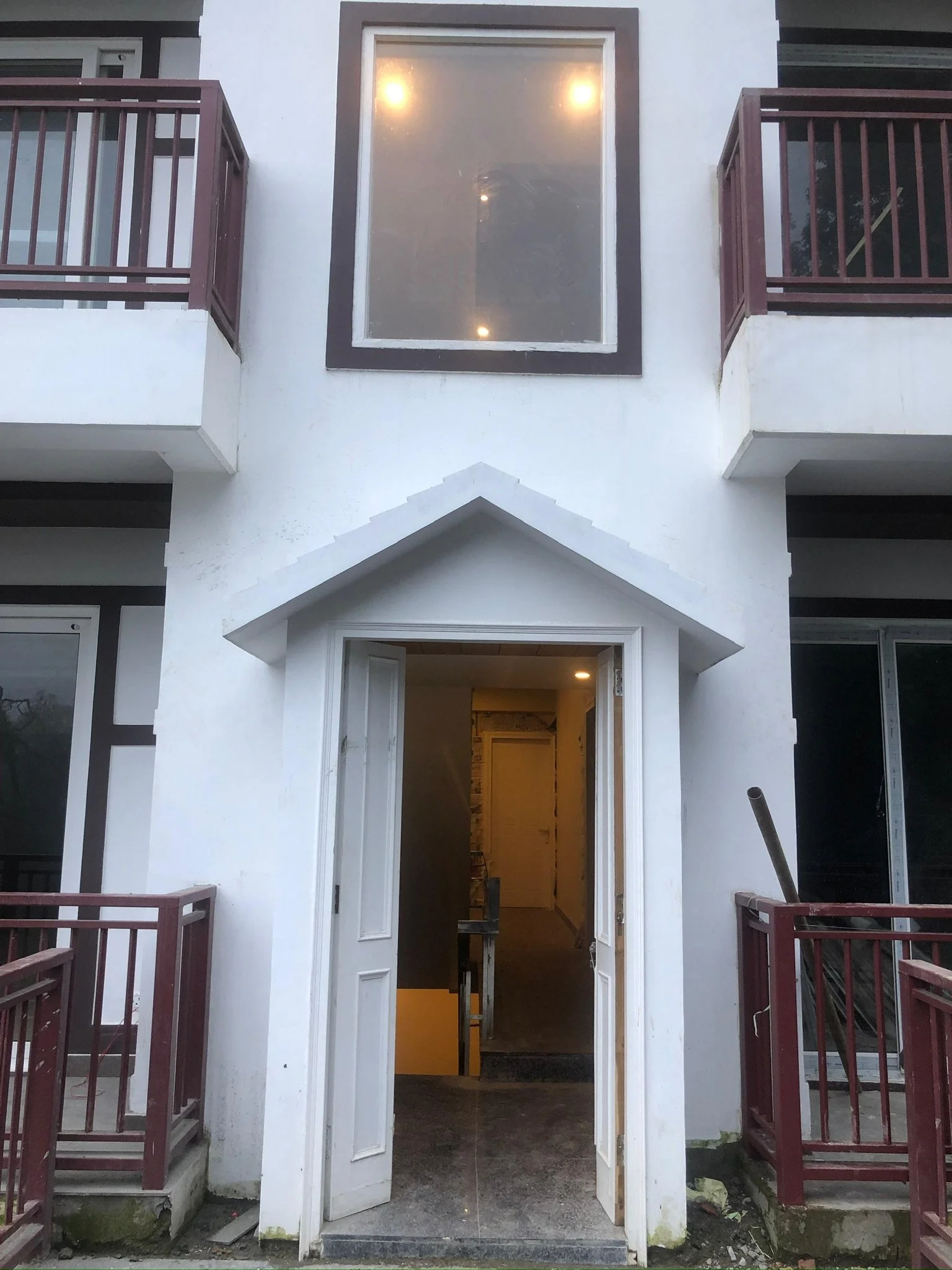 The image shows the entrance to a building with open double doors, leading to an interior stairway. Above the entrance, there is a large window with lights on inside. The building has white exterior walls with dark framing around the windows and a sm