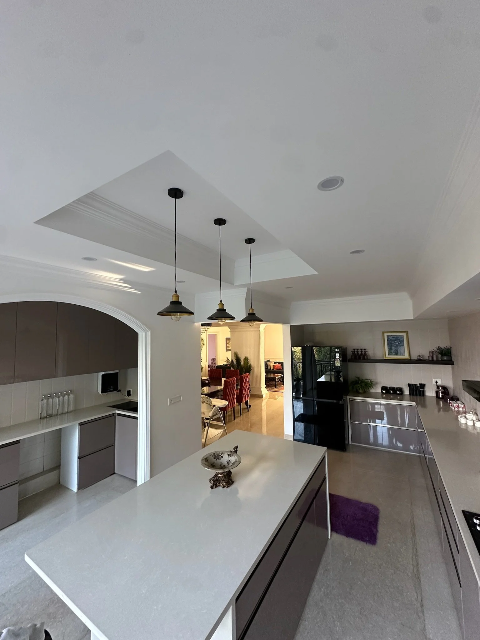 Small kitchenette with black sink, beige cabinets, purple towel, wall-mounted soap dispenser, and bright overhead lighting.