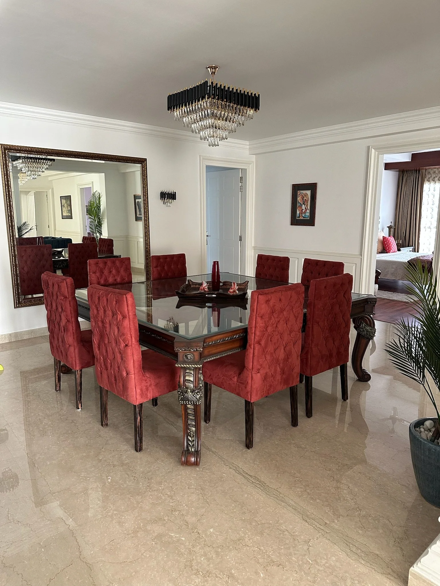 Luxury living room with marble flooring, white walls, and high ceilings with crown molding. Blue and red furniture, green potted plant, and large windows allowing natural light.