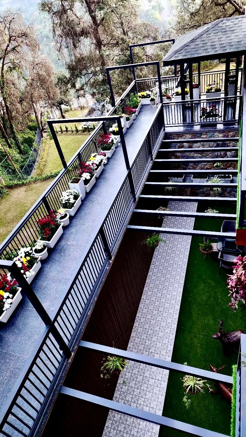 View of a balcony with a railing decorated with flower pots, stairs leading down, and a garden with trees and a pathway.