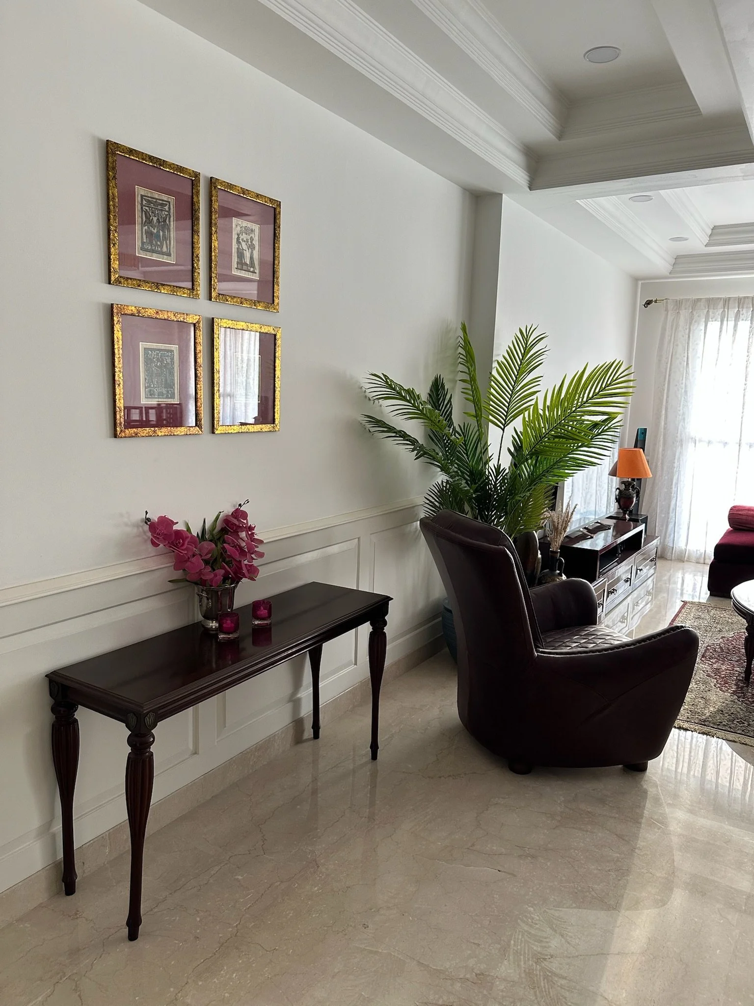 Indoor lounge with a black pool table set up for billiards, positioned under a modern chandelier with multiple hanging glass lights, surrounded by armchairs, plants, and decorative wall art.