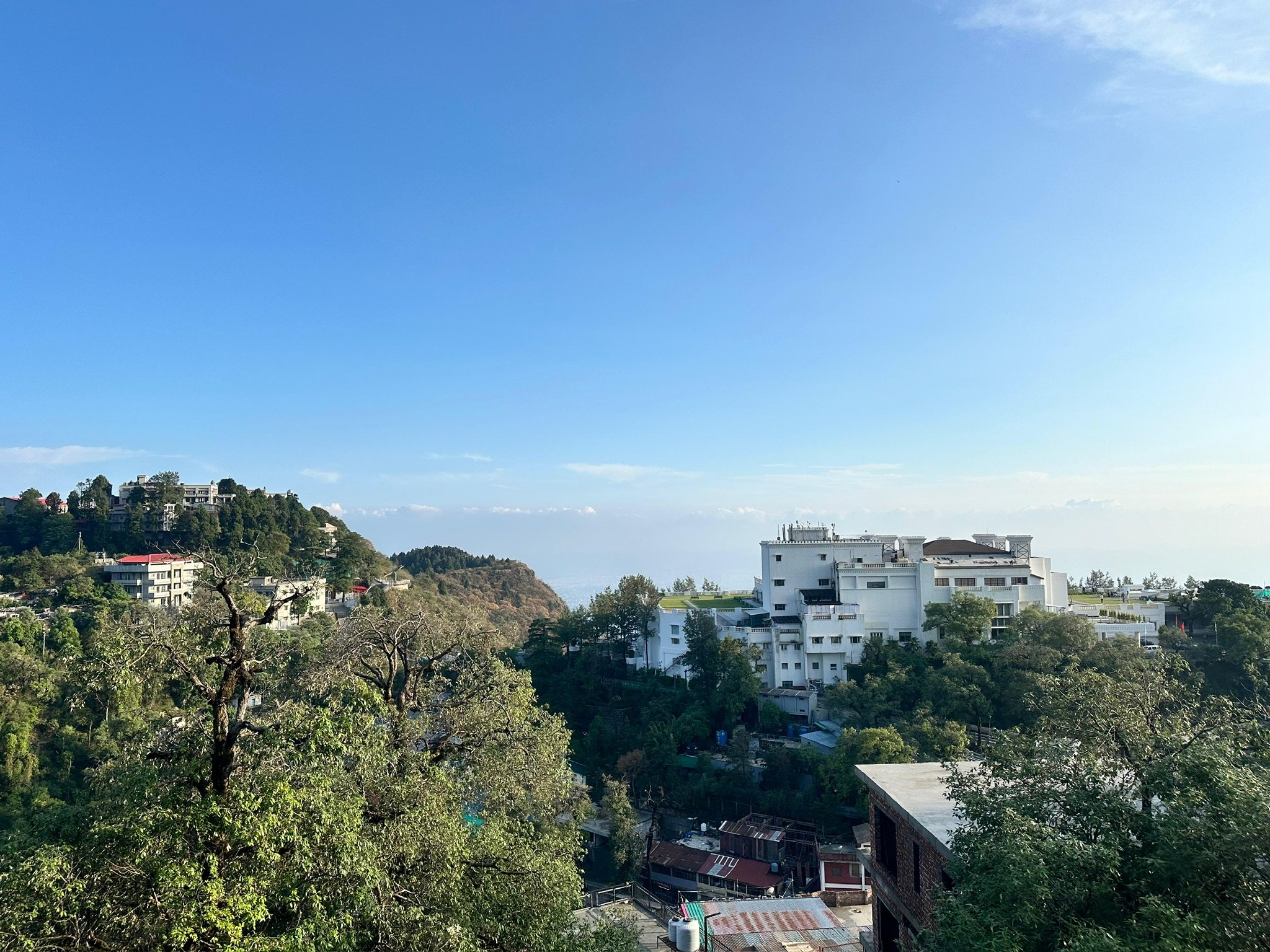 A scenic view of hills with residential buildings and lush greenery under a bright blue sky.