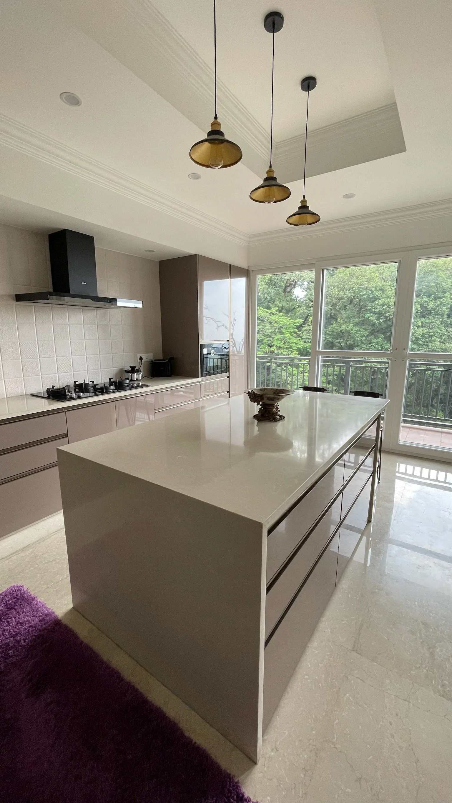 Modern kitchen with beige tiled walls and a shiny black refrigerator on the left. A white countertop with beige and purple cabinetry below. A black shelf with plants and art on top, and various cups and jars on the counter.